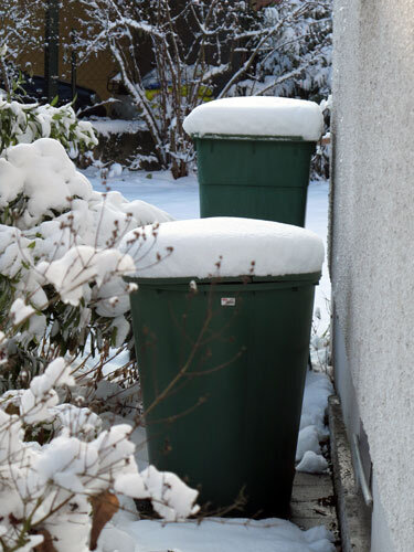 Deux récupérateurs d'eau verts couverts de neige contre le mur en hiver