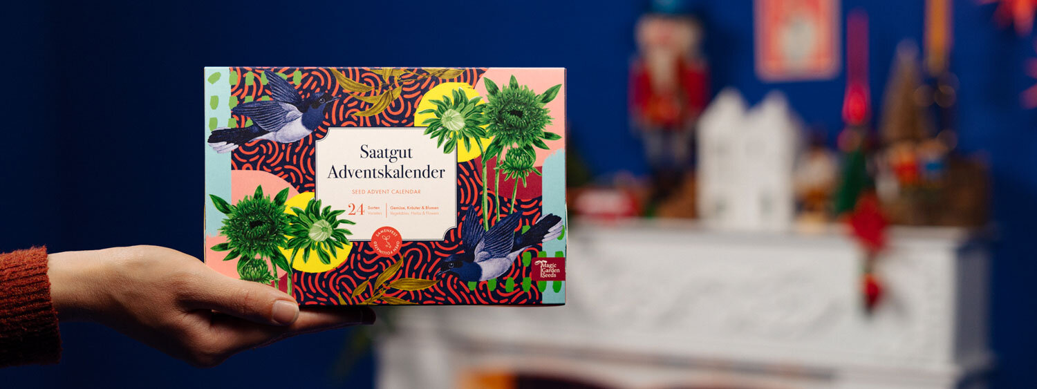 Calendrier de l'Avent de graines « Légumes, herbes aromatiques & fleurs » tenu devant une cheminée décorée pour Noël