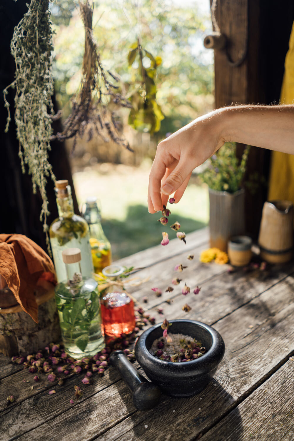 Boutons de fleurs séchés versés dans un mortier, à côté d'huiles aux herbes et de bouquets suspendus