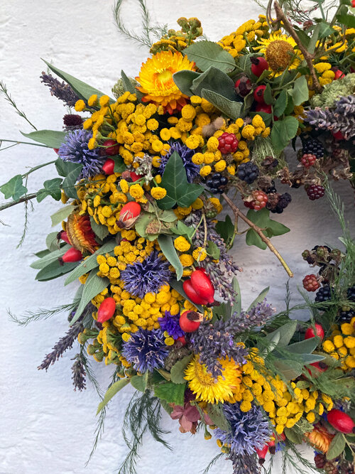Détail d'une couronne d'automne avec fleurs jaunes et bleues, cynorrhodons rouges et baies sombres