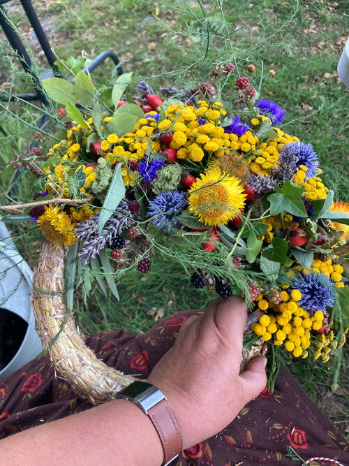 Couronne d'automne à moitié liée : fleurs jaunes et bleues, graminées et baies sur base en paille