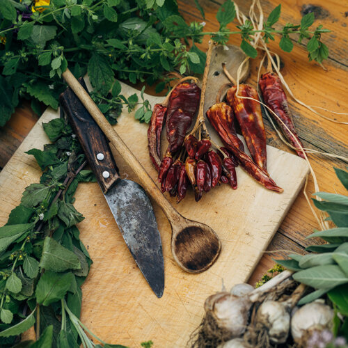 Piments séchés, herbes fraîches et ail sur une planche avec couteau et cuillère en bois