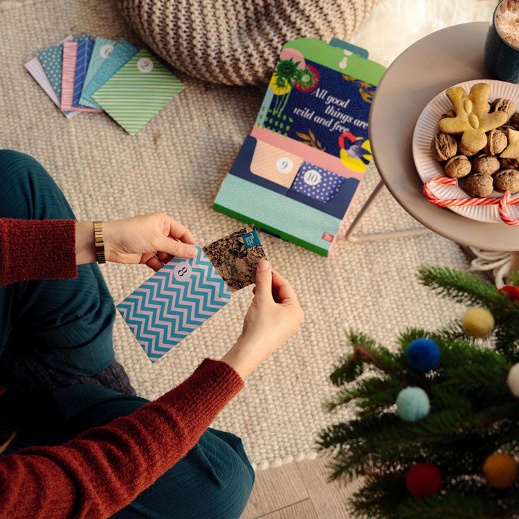 Personne ouvrant un sachet de graines du calendrier de l'Avent, à côté de biscuits et d'un sapin