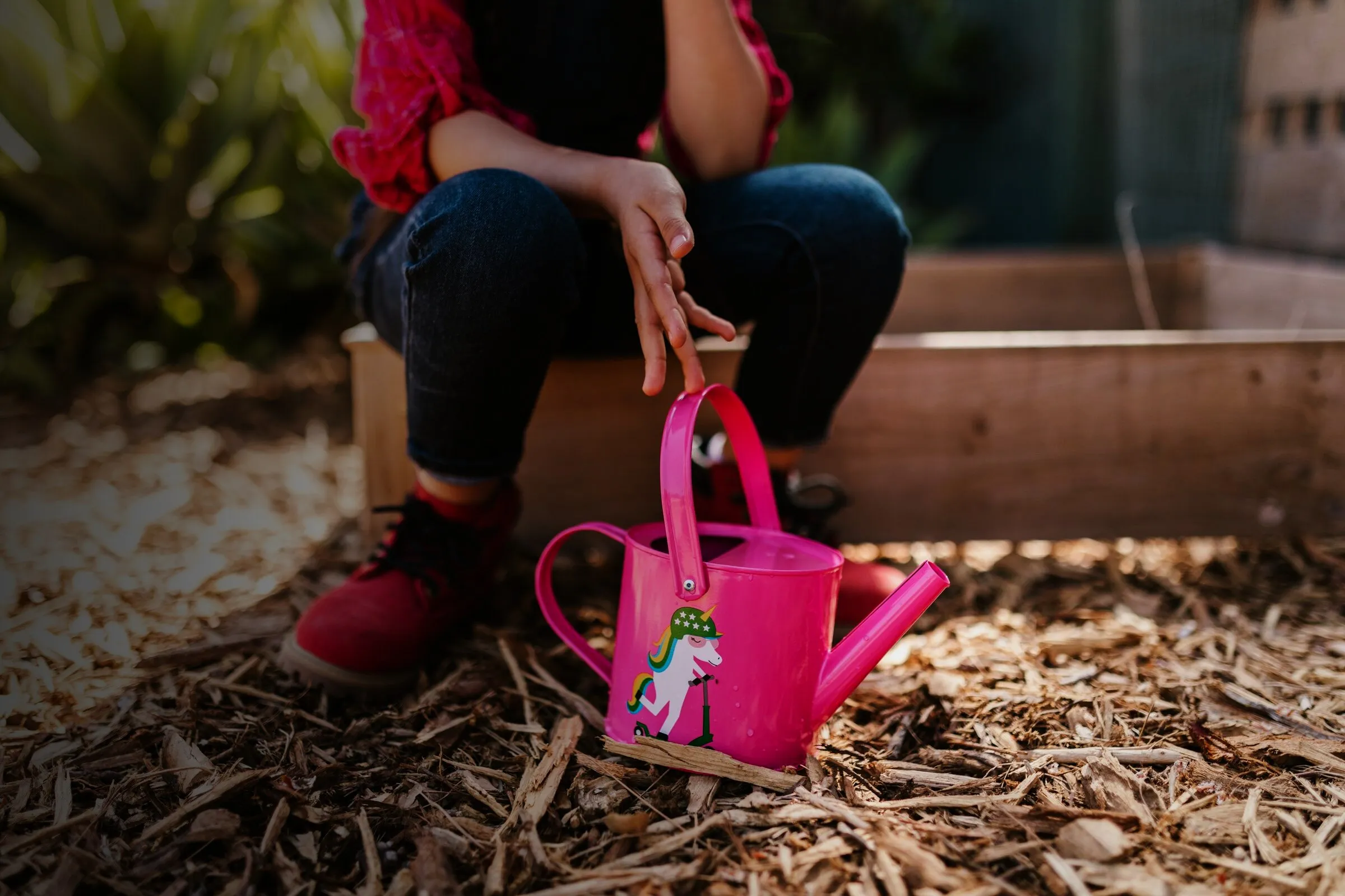 Kind in Gummistiefeln mit pinker Gießkanne im Garten