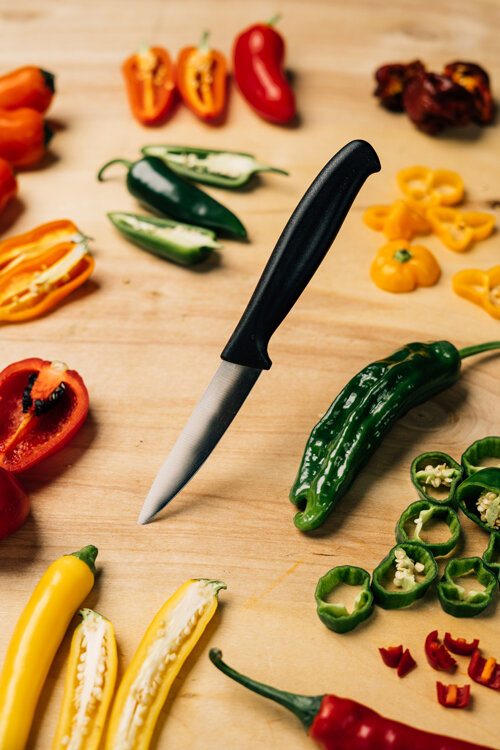 Piments coupés rouges, jaunes, orange et verts avec un couteau sur une planche